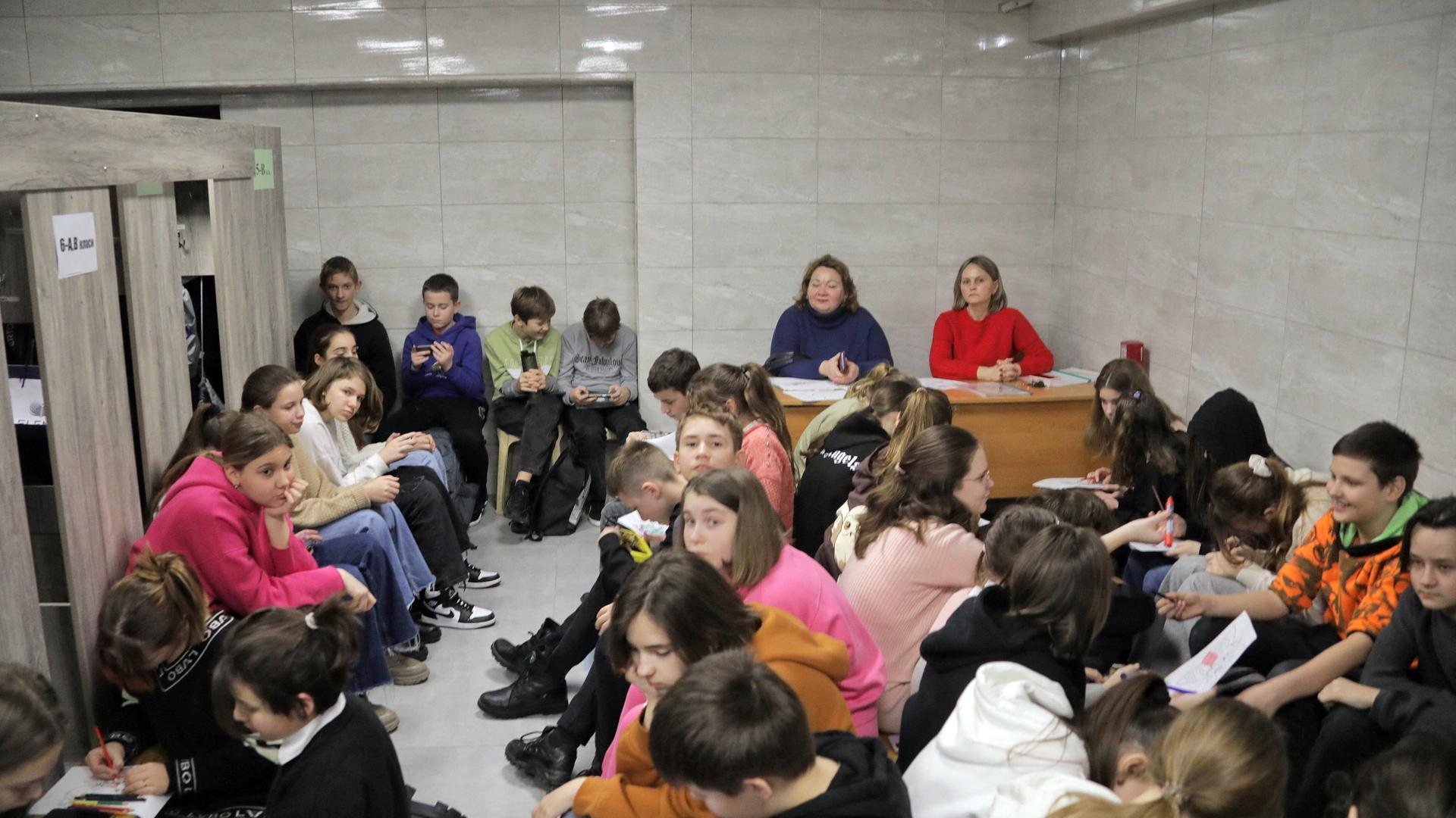 Schülerinnen und Schüler werden  während eines Luftalarms in einem Bombenschutzkeller ihrer Schule unterrichtet.