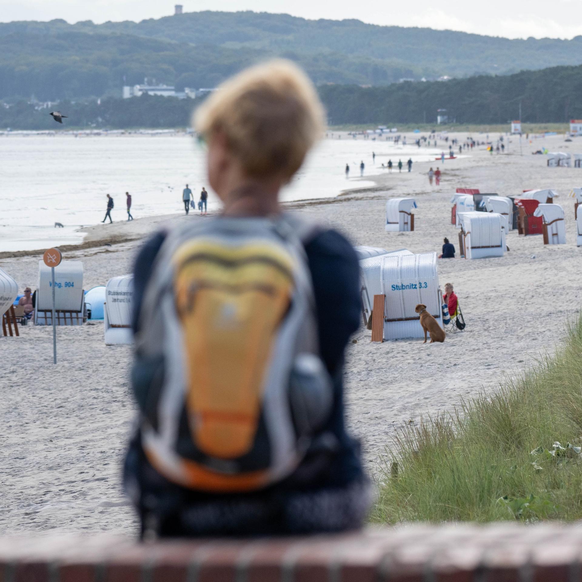 Blick auf den Strand von Prora. Vorne, auf einer Mauer sitzen zwei Menschen.