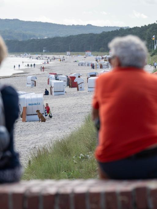 Blick auf den Strand von Prora. Vorne, auf einer Mauer sitzen zwei Menschen.