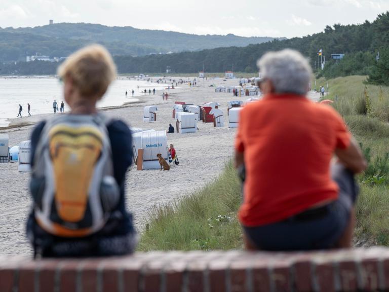 Blick auf den Strand von Prora. Vorne, auf einer Mauer sitzen zwei Menschen.