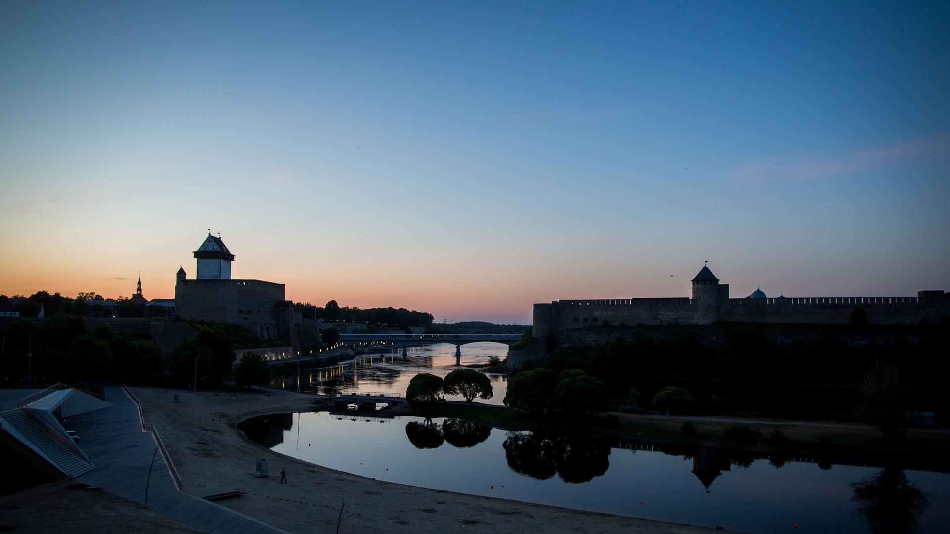 Die Sonne geht hinter der Hermannsfeste in der estnischen Stadt Narva und der russischen Burg Iwangorod auf der gegenüberliegenden Seite unter. Dazwischen fließt der Fluss Narva.