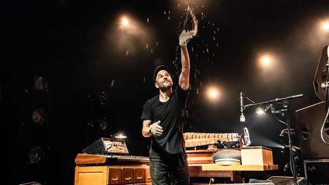 Der deutsche Musiker, Pianist und Komponist Nils Frahm bei einem Live-Konzert in Kopenhagen, umgeben von seinen vielen Instrumenten. Er wirft Sandglitzer in die Luft.