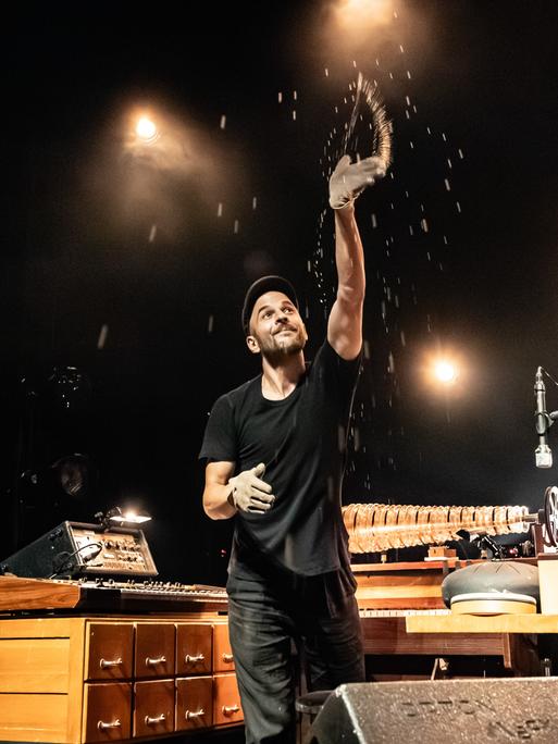 Der deutsche Musiker, Pianist und Komponist Nils Frahm bei einem Live-Konzert in Kopenhagen, umgeben von seinen vielen Instrumenten. Er wirft Sandglitzer in die Luft.