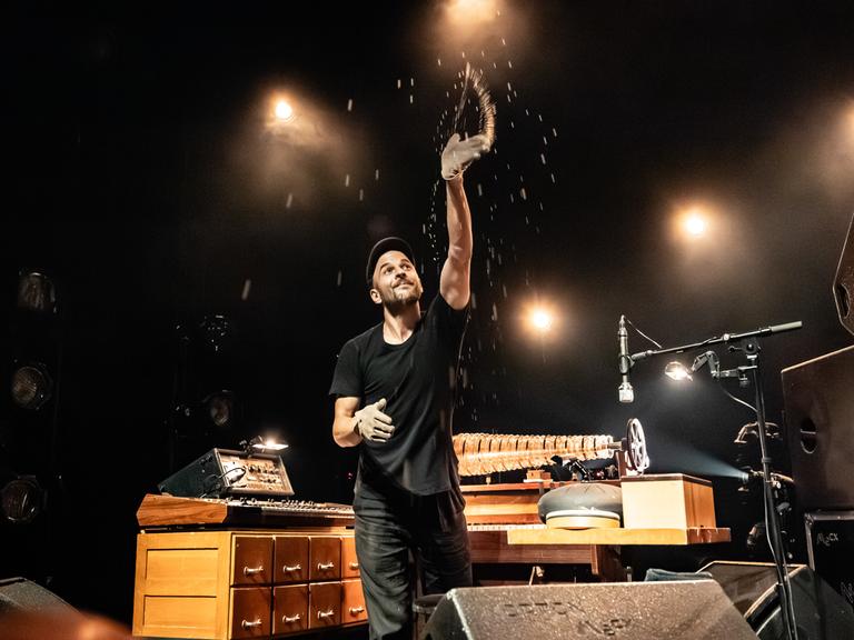 Der deutsche Musiker, Pianist und Komponist Nils Frahm bei einem Live-Konzert in Kopenhagen, umgeben von seinen vielen Instrumenten. Er wirft Sandglitzer in die Luft.
