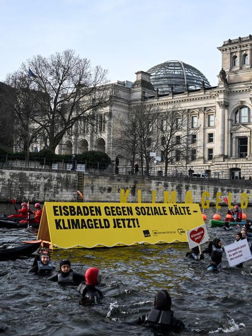 Vor dem Reichstag in Berlin schwimmen Personen in der Spree und halten ein Banner und Plakate in der Hand.