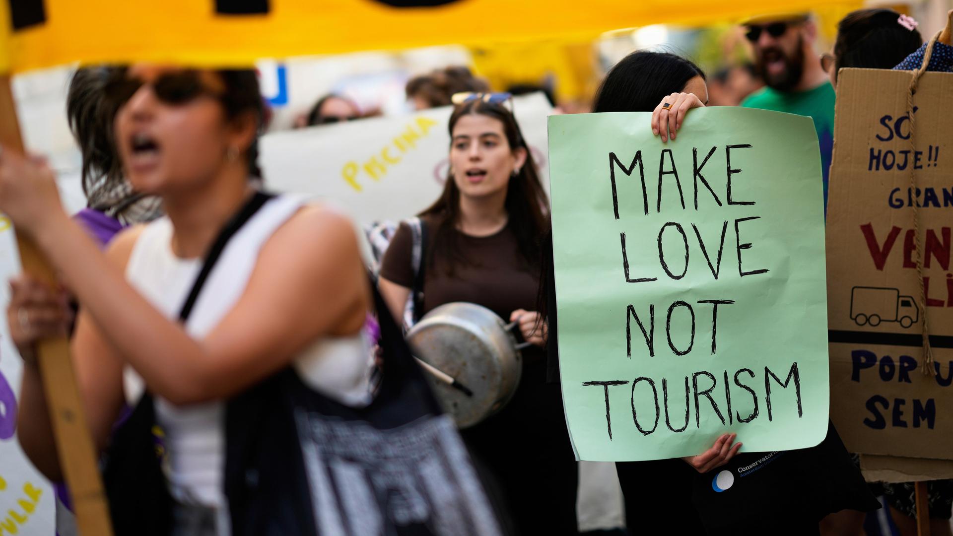 Demonstrierende stehen dicht an dicht bei einer Kundgebung gegen Übertourismus in Lissabon, auf einem Plakat steht der Schriftzug "Make Love Not Tourism".