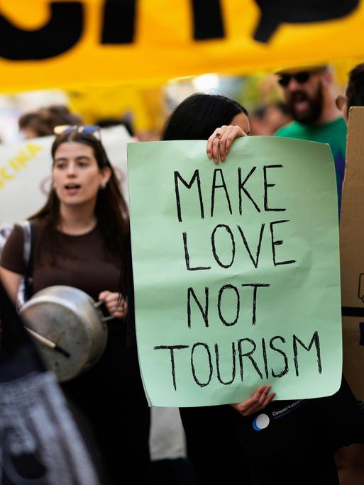 Demonstrierende stehen dicht an dicht bei einer Kundgebung gegen Übertourismus in Lissabon, auf einem Plakat steht der Schriftzug "Make Love Not Tourism".