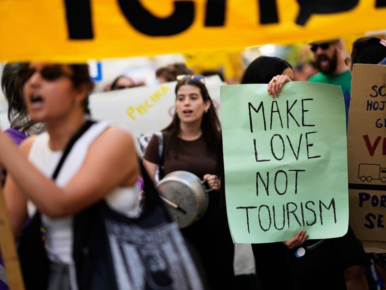 Demonstrierende stehen dicht an dicht bei einer Kundgebung gegen Übertourismus in Lissabon, auf einem Plakat steht der Schriftzug "Make Love Not Tourism".