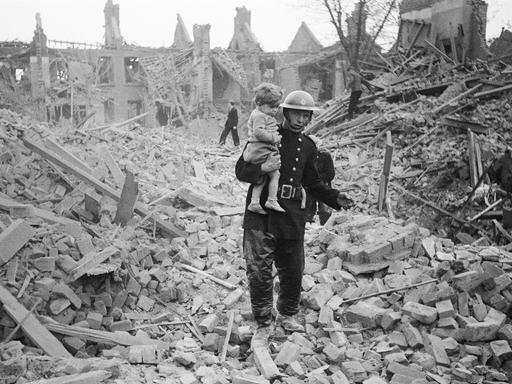 Ein Feuerwehrmann trägt ein Kleinkind nach einem Bombenangriff aus den Trümmern, London, um 1940. 
