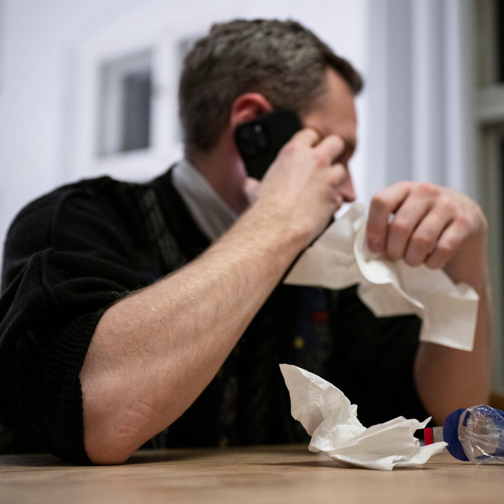 Ein Mann hält ein Taschentuch in einer Hand und ein Telefon in der Anderen. Der Gemeinsame Bundesausschuss entscheidet über dauerhafte Möglichkeiten zu telefonischen Krankschreibungen. Patientinnen und Patienten sollen sich bei leichteren Erkrankungen künftig generell telefonisch von ihrer Arztpraxis krankschreiben lassen können. Der Gemeinsame Bundesausschuss von Ãrzten, Krankenkassen und Kliniken will am 7. Dezember über eine Ãnderung der entsprechenden Arbeitsunfähigkeits-Richtlinie entscheiden.