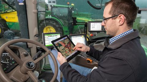 Ein Landwirt Florian sitzt am Steuer eines Treckers mit einem Tablet in der Hand. 