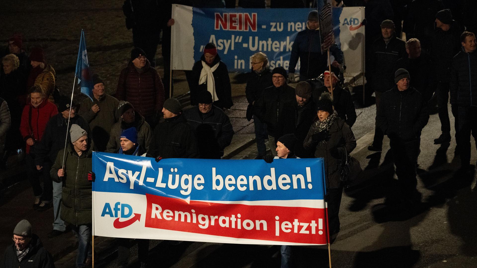 Dresden: Teilnehmer einer Demonstration der rechtsextremistischen Bewegung Pegida laufen am Abend am Terrassenufer entlang und tragen Banner der AfD mit der Aufschrift "Asyl-Lüge beenden!