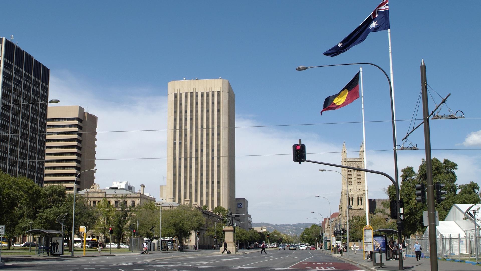 Die St. Francis Kirche in Adelaid in Australien. Ein Stück die Straße davor stehen Masten mit wehenden australischen und Aborigine-Fahnen.