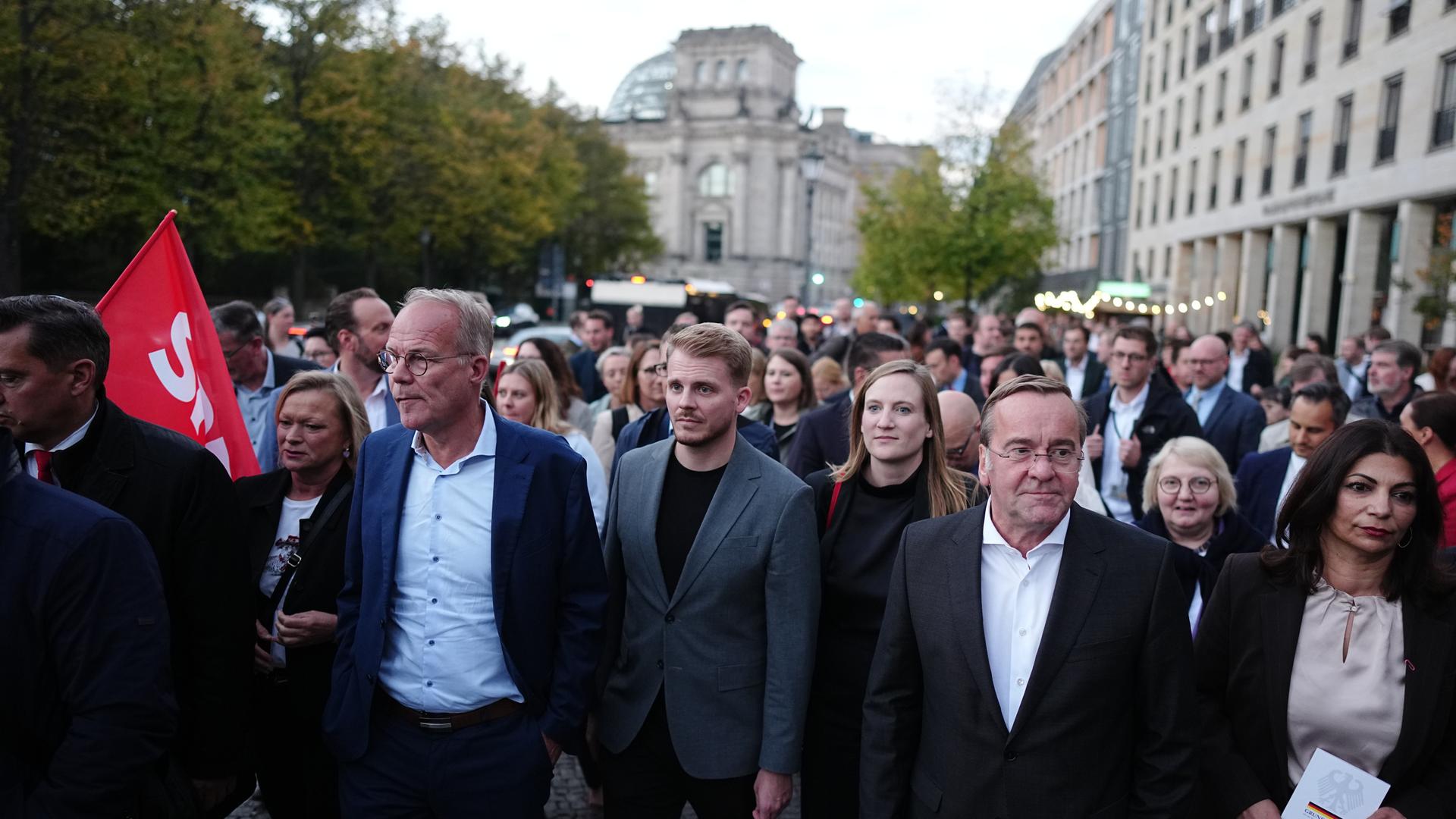 Abgeordnete der SPD gehen über eine Straße in Berlin. Im Hintergrund ist das Reichstagsgebäude zu erkennen.