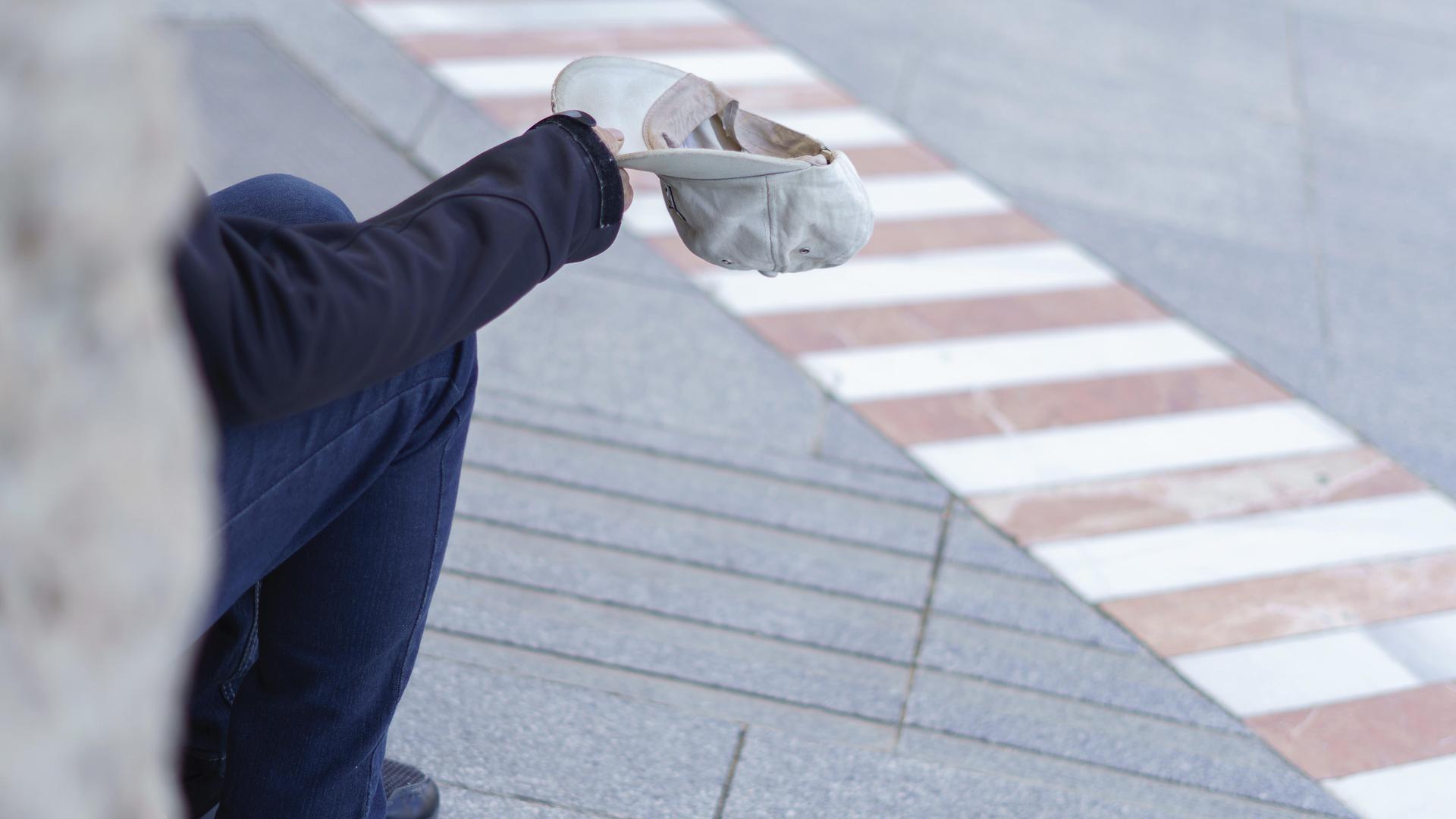 Eine Person sitzt auf einem Gehweg und bittet um eine Spende.