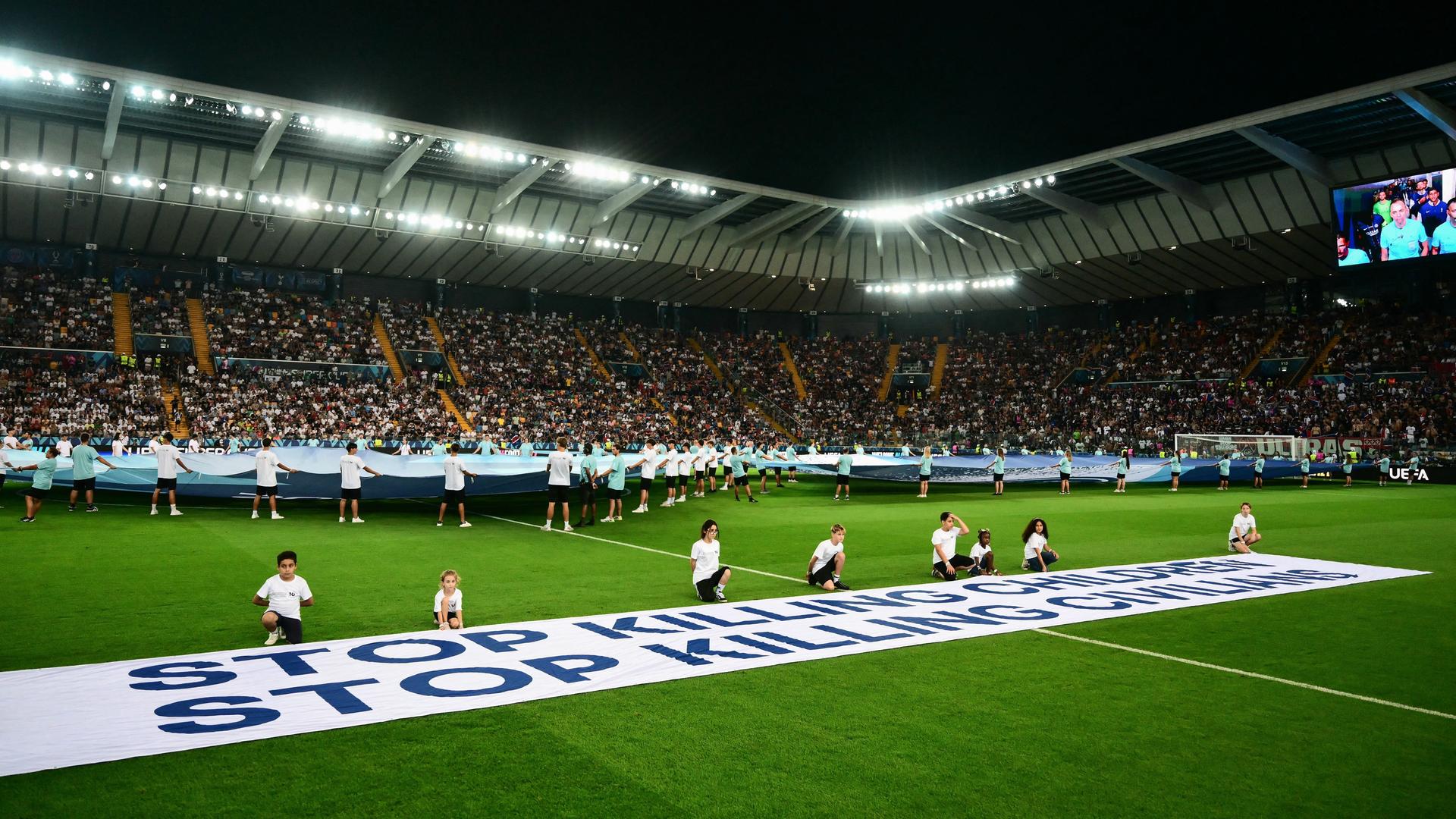 Ballkinder halten ein Banner im Stadion, auf dem steht: "Hört auf, Kinder zu töten" und "Hört auf, Zivilisten zu töten".