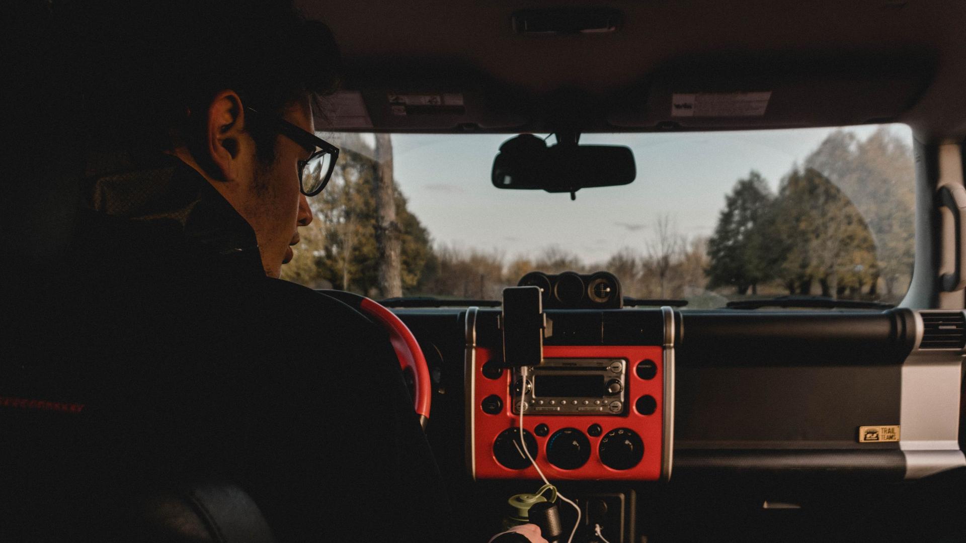 Ein Mann sitzt in einer einsamen Waldgegend allein im Auto und blickt auf sein Autoradio.