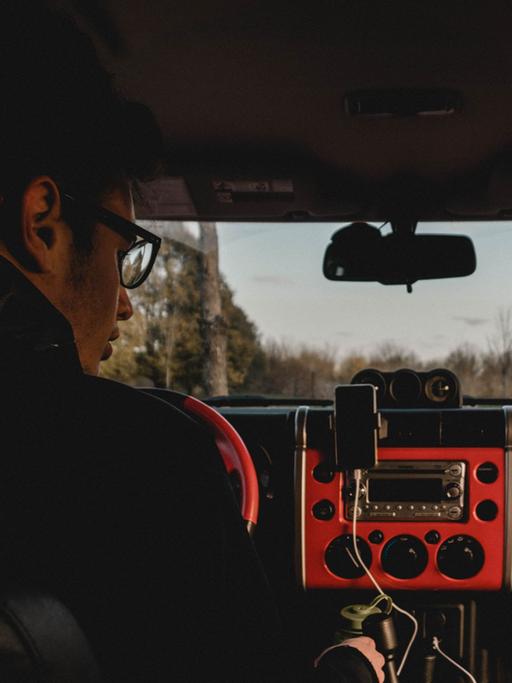 Ein Mann sitzt in einer einsamen Waldgegend allein im Auto und blickt auf sein Autoradio.