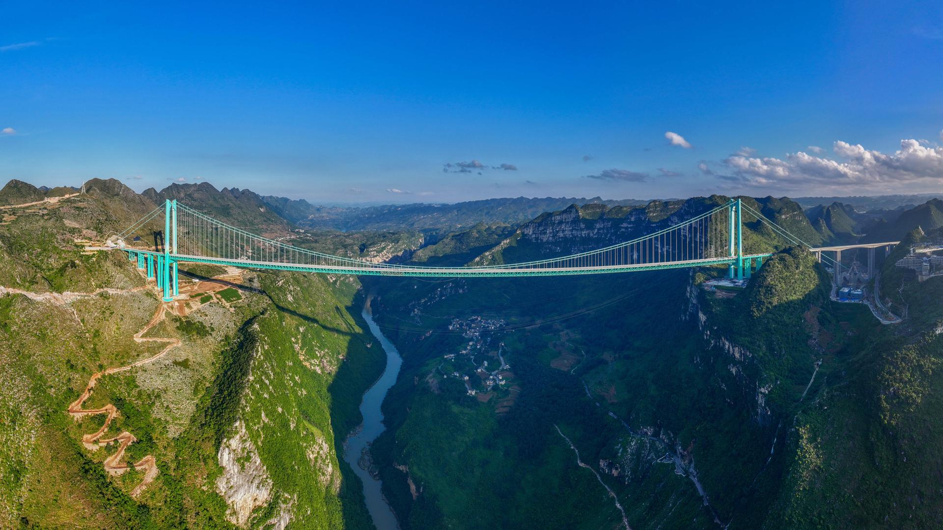 Die Huajiang Canyon Bridge über einer tiefen Schlucht, im Hintergrund blauer Himmel