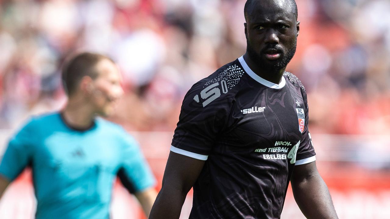 Raphael Assibey-Mensah im schwarzen Trikot vorn Rot-Weiß Erfurt während eines Spielszene. Im Hintergrund ist unscharf der Schiedsrichter zu sehen. 