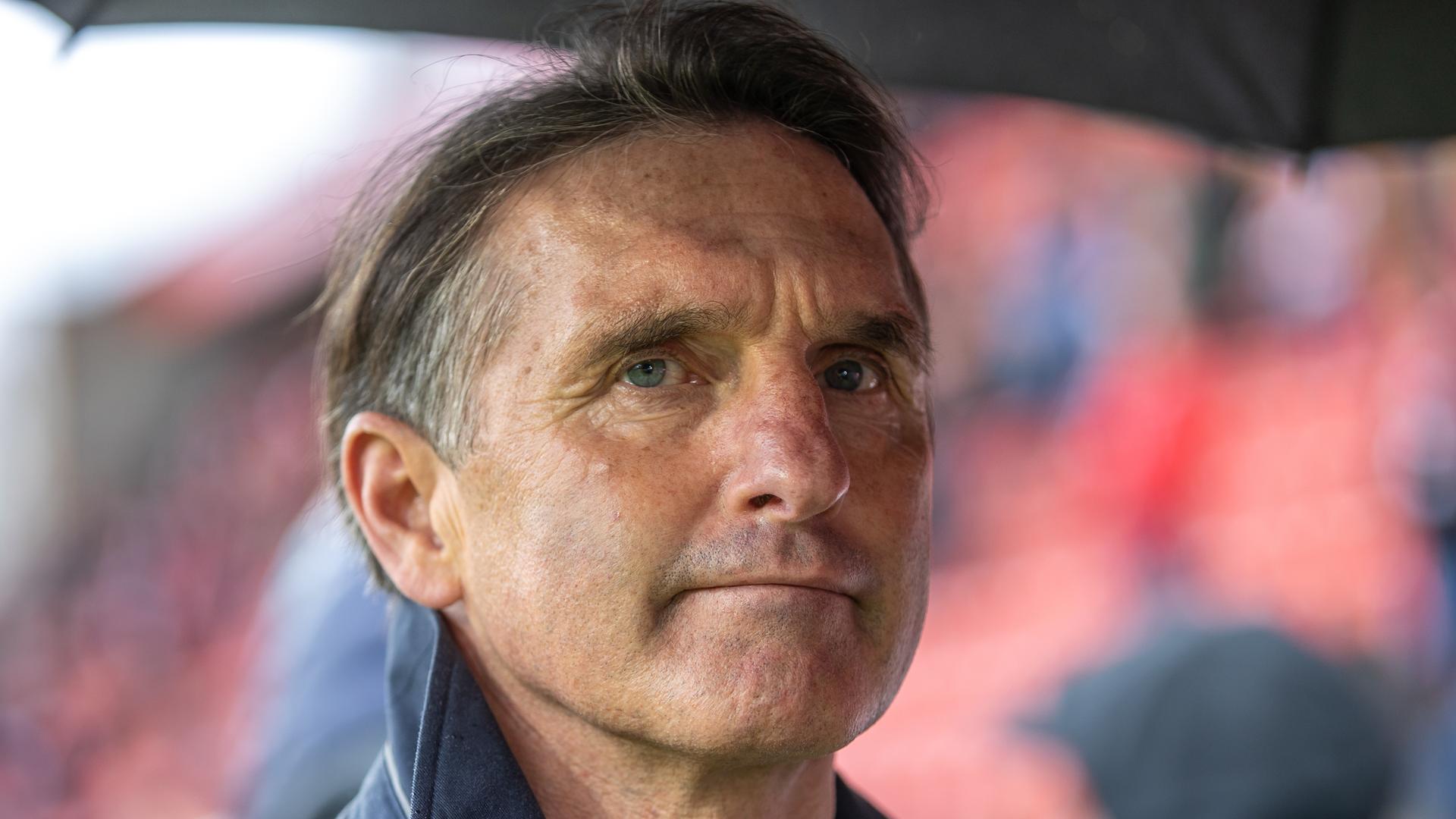 Der Fußball-Trainer Bruno Labbadia. Ein Mann mit graumelierten Haaren steht unter einem Regenschirm. Er blickt mit zusammengenkiffenen Lippen in die Kamera. Der Fußball-Trainer Bruno Labbadia. Ein Mann mit graumelierten Haaren steht unter einem Regenschirm. Er blickt mit zusammengenkiffenen Lippen in die Kamera.