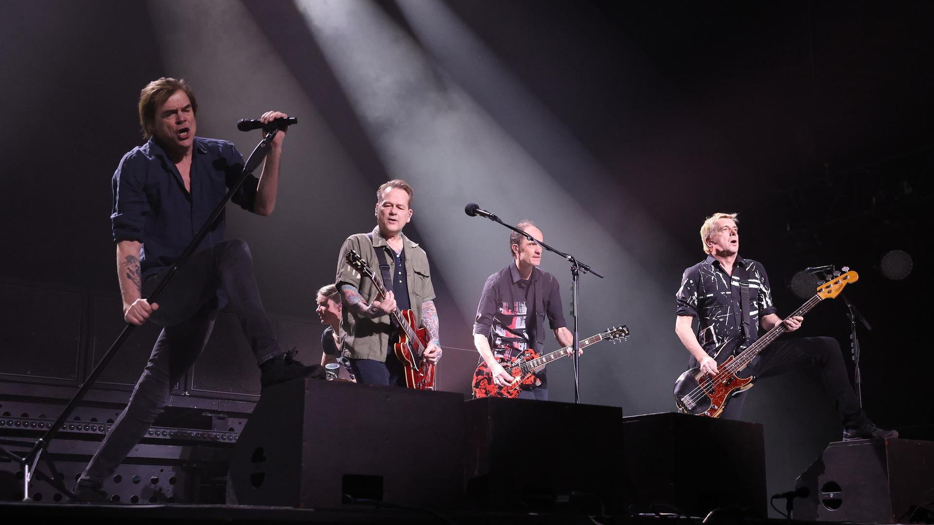 Die Toten Hosen stehen nebeneinander auf einer Bühne mit schwarzem Hiintergrund
