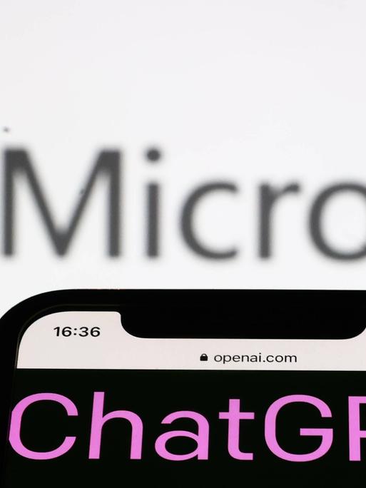 Ein Smartphone mit dem Wort ChatGPT auf dem Screen wird auf einen Bildschirm gerichtet, auf dem das Logo und der Schiftzug der Firma Microsoft zu sehen sind.