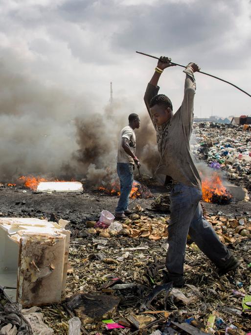 Junge afrikanische Männer verbrennen Elektroschrott auf einer Mülldeponie.