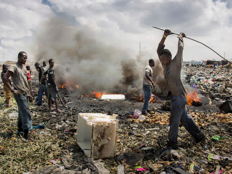 Junge afrikanische Männer verbrennen Elektroschrott auf einer Mülldeponie.