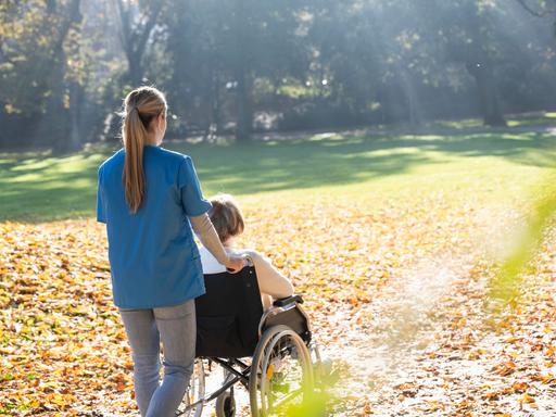 Eine Frau schiebt eine in einem Rollstuhl sitzende Frau in einem Park