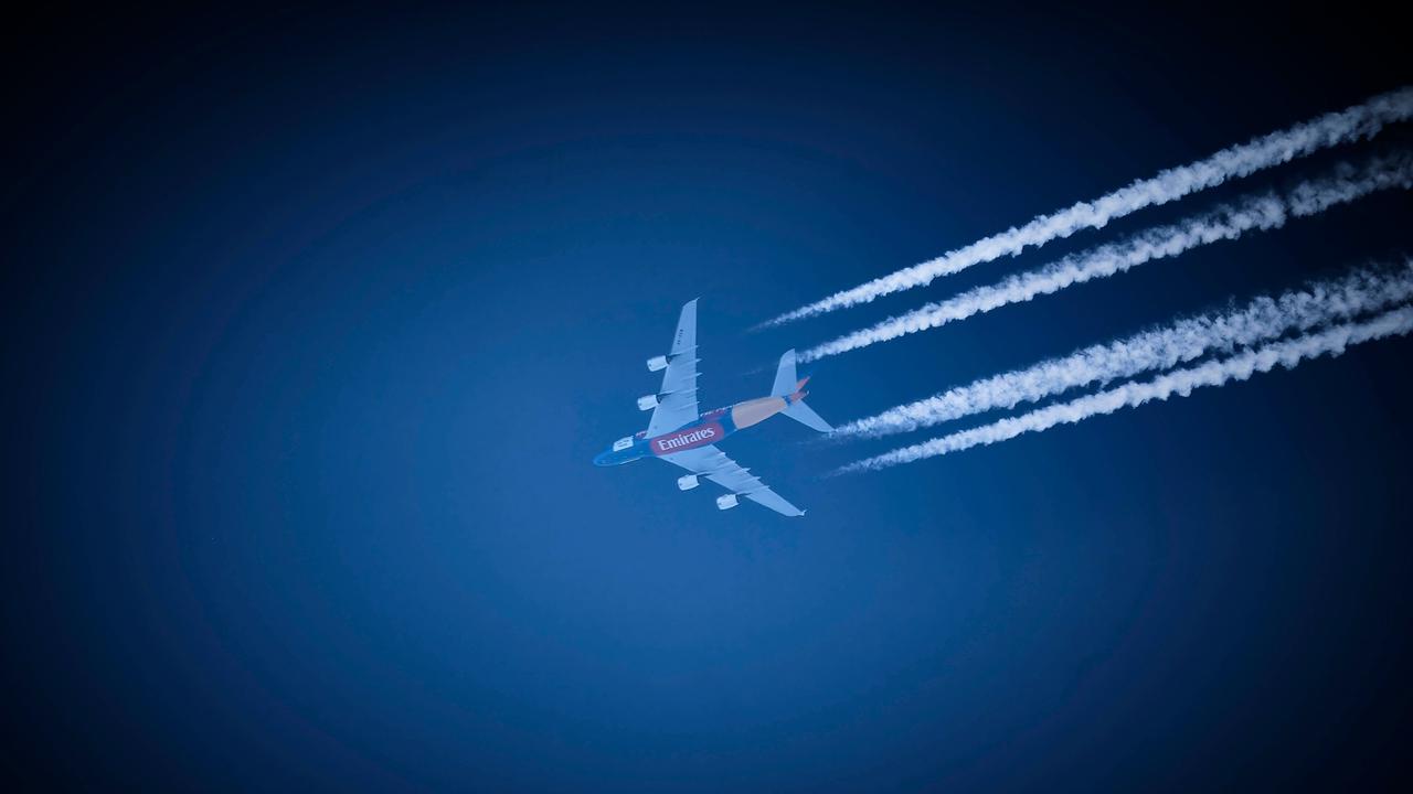Ein Verkehrsflugzeug der Fluggesellschaft Emirates hinterlässt am strahlend blauen Himmel Kondensstreifen. 
