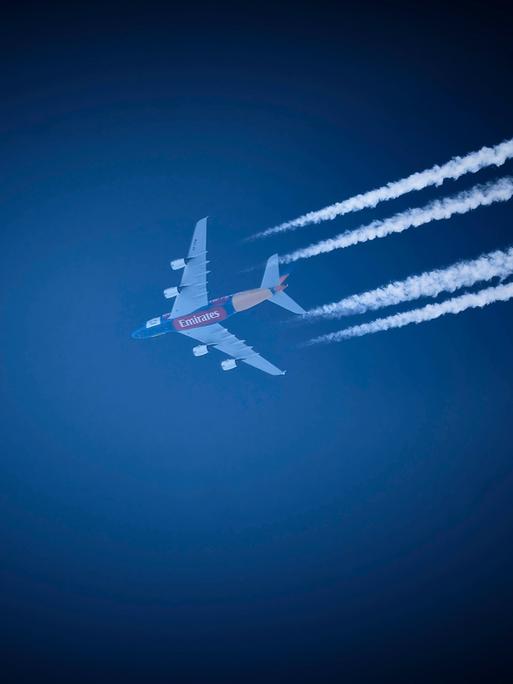 Ein Verkehrsflugzeug der Fluggesellschaft Emirates hinterlässt am strahlend blauen Himmel Kondensstreifen. 