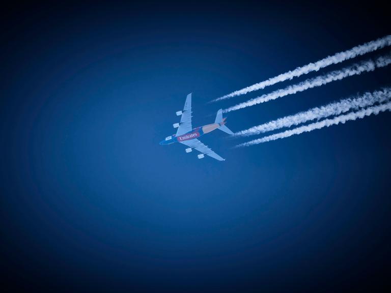 Ein Verkehrsflugzeug der Fluggesellschaft Emirates hinterlässt am strahlend blauen Himmel Kondensstreifen. 