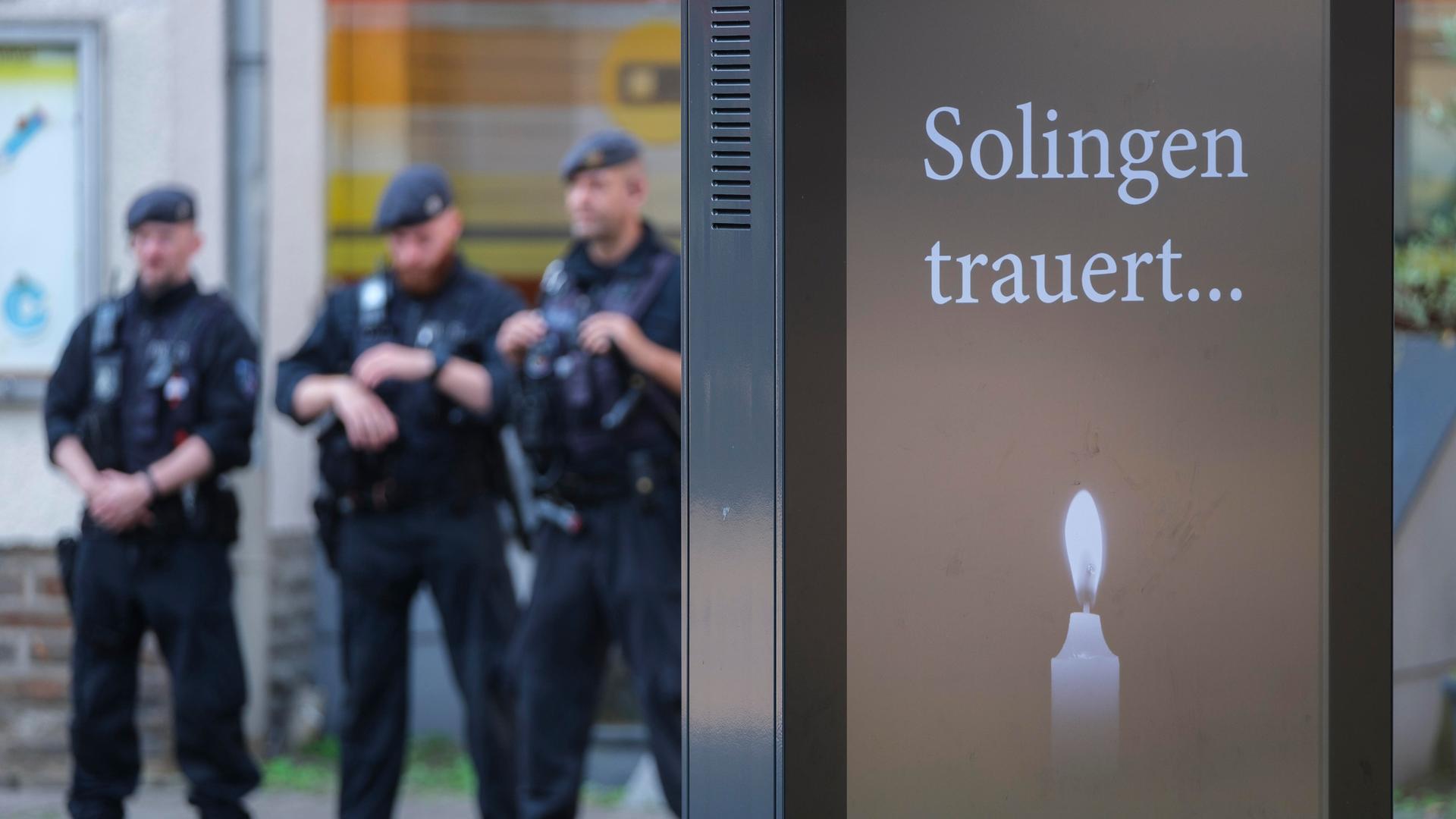 Polizisten stehen hinter einer Anzeigentafel "Solingen trauert..." mit Kerze im Gedenken an die Opfer des Attentats von Solingen am Tatort Fronhof am 01.09.2024.