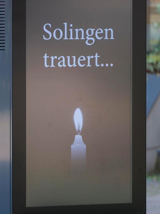 Polizisten stehen hinter einer Anzeigentafel "Solingen trauert..." mit Kerze im Gedenken an die Opfer des Attentats von Solingen am Tatort Fronhof am 01.09.2024.