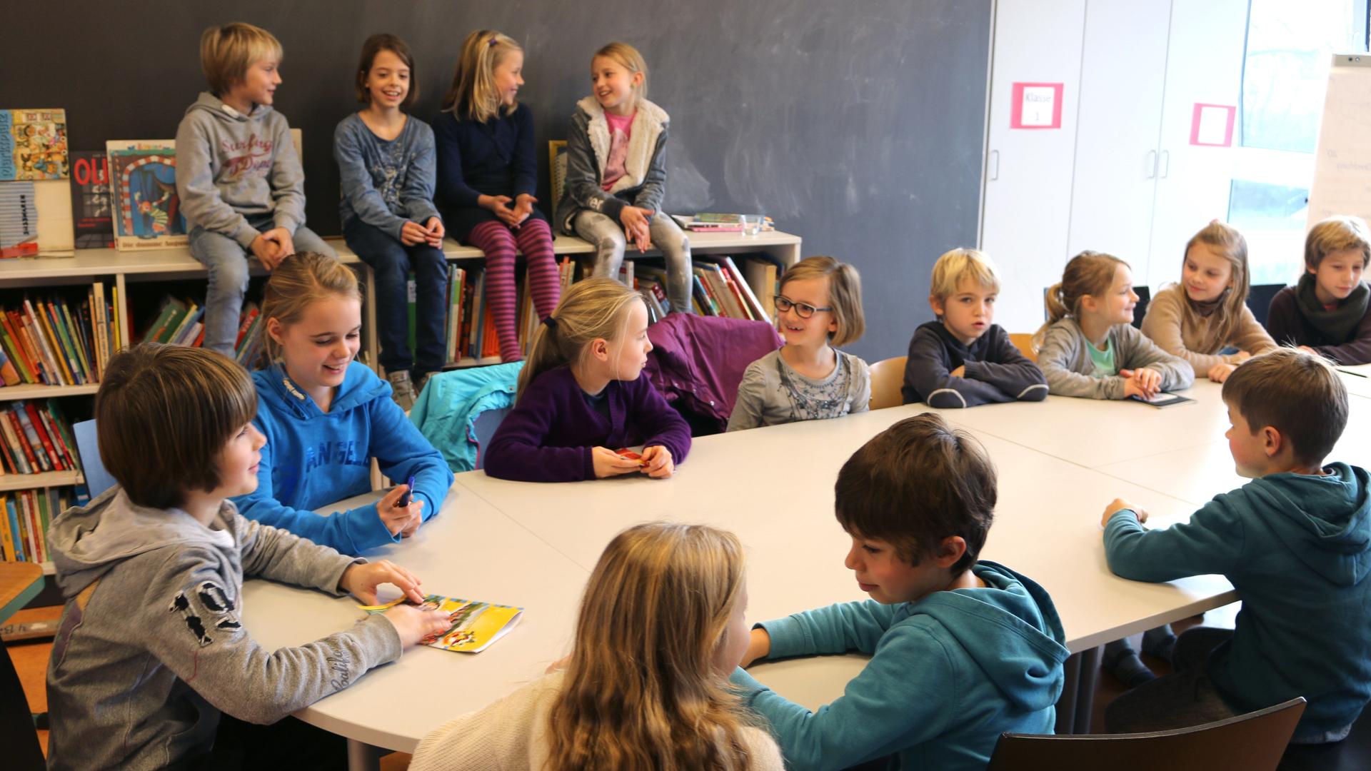 Kinder in einem Kinderparlament an einer Schule sitzen an einem runden Tisch, die Klassensprecherinnen treffen sich und besprechen verschiedene Probleme.