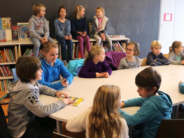 Kinder in einem Kinderparlament an einer Schule sitzen an einem runden Tisch, die Klassensprecherinnen treffen sich und besprechen verschiedene Probleme.