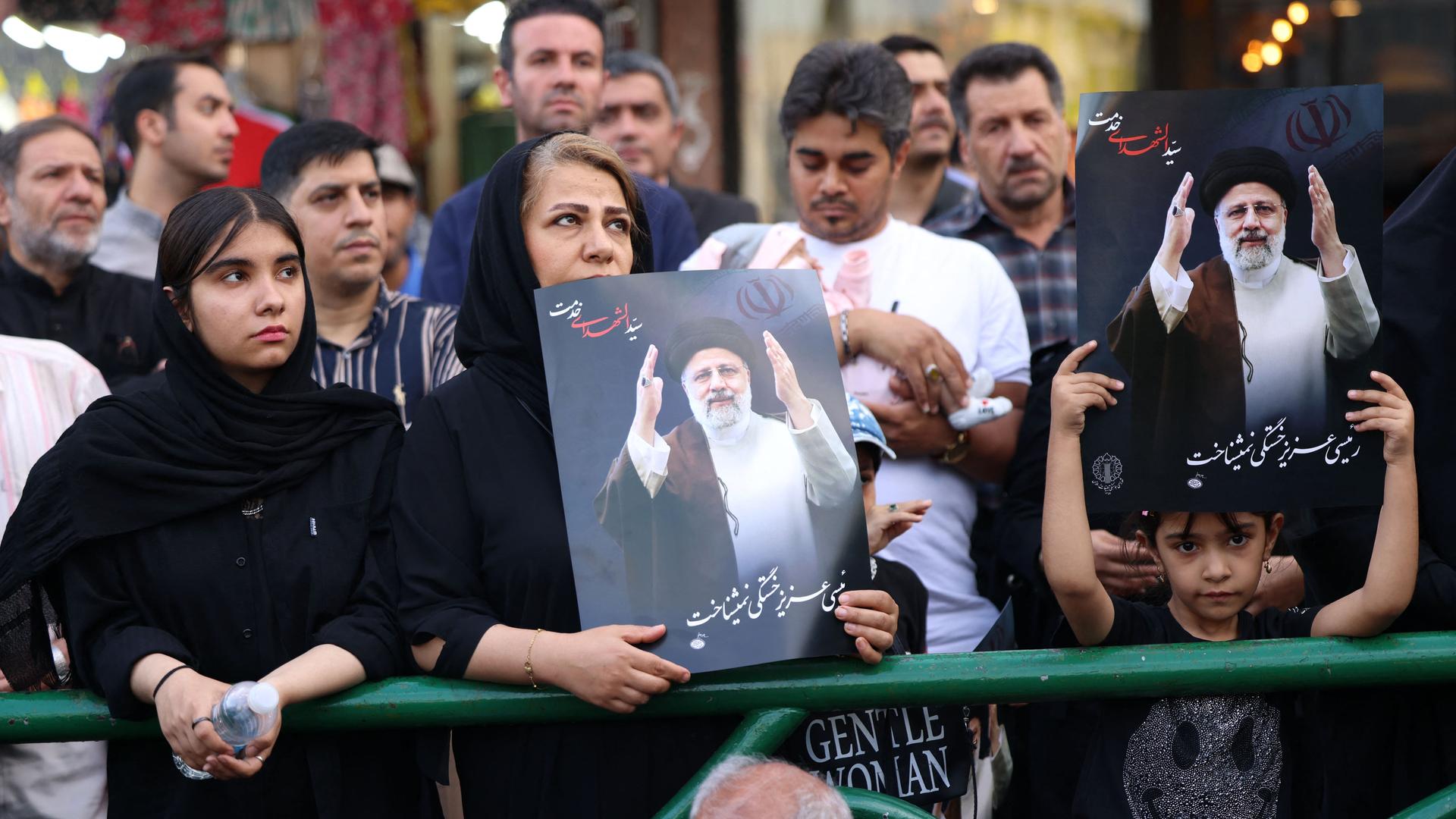 Menschen im Iran stehen dicht beieinander. Eine Frau und ein Mädchen tragen Bilder des verstorbenen Präsidenten Raisi.