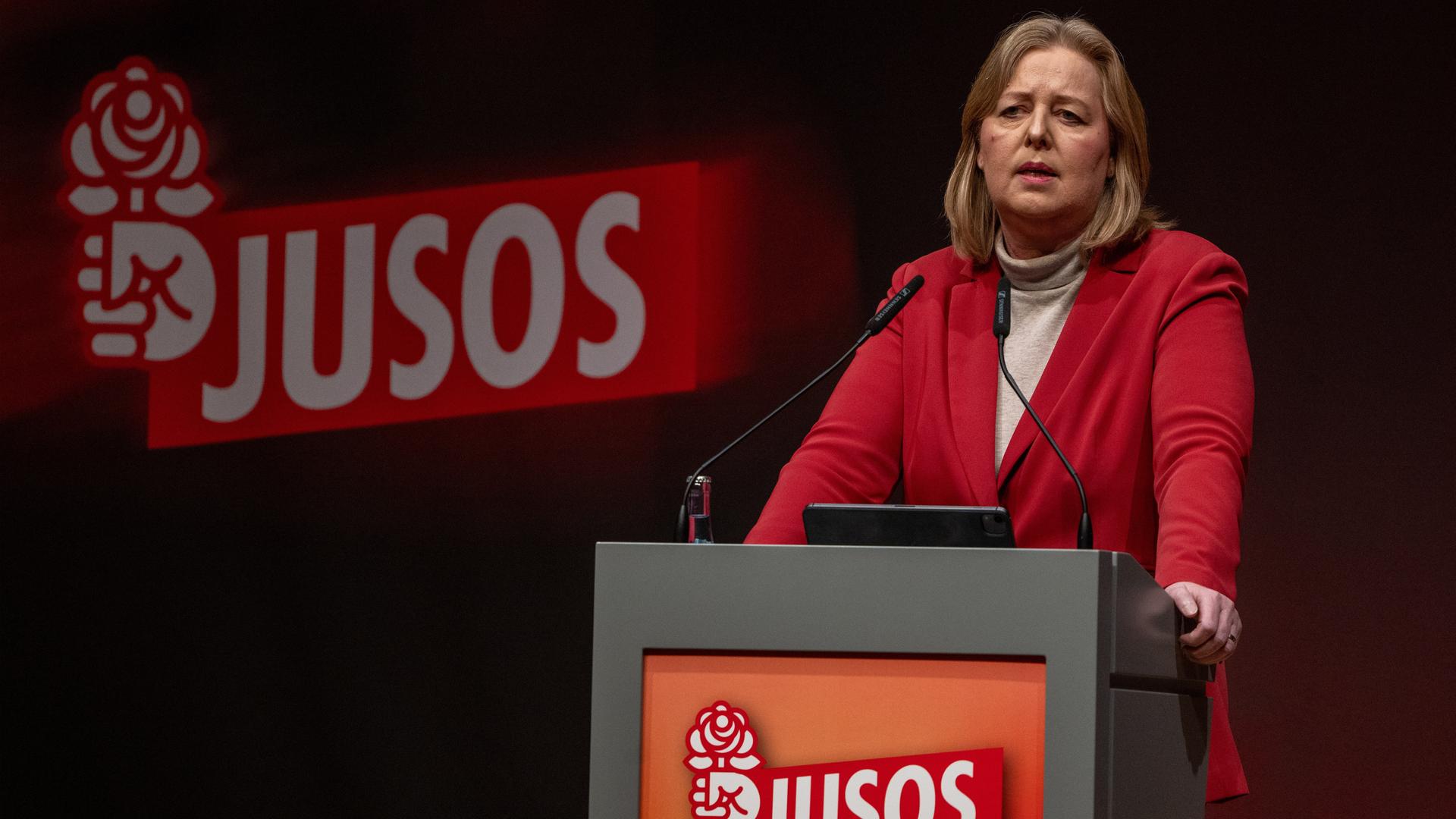 Bärbel Bas steht am Rednerpult der Jusos. Deren Parteilogo zeigt eine Hand mit einer Rose. 