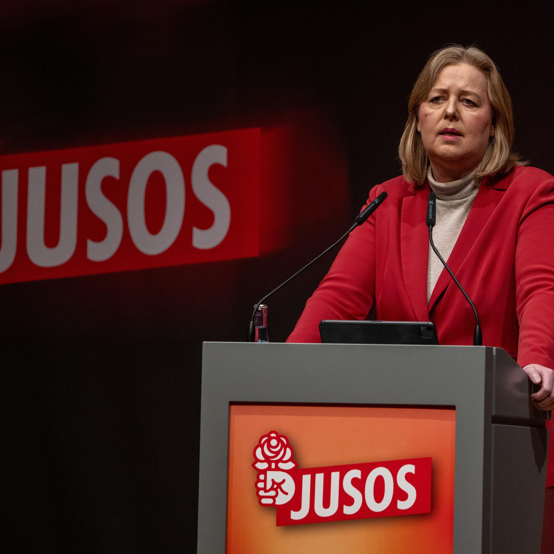 Bärbel Bas steht am Rednerpult der Jusos. Deren Parteilogo zeigt eine Hand mit einer Rose.