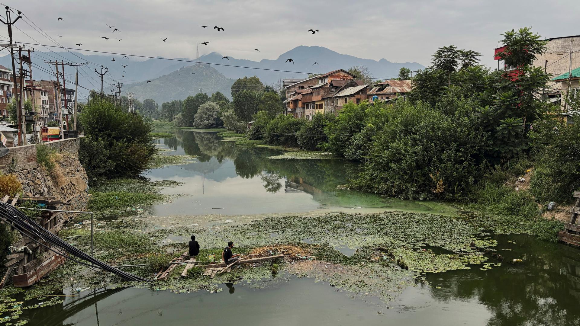 Menschen stehen an einem von der Sturzflut zerstörten und überfluteten Kanal in Kashmir.