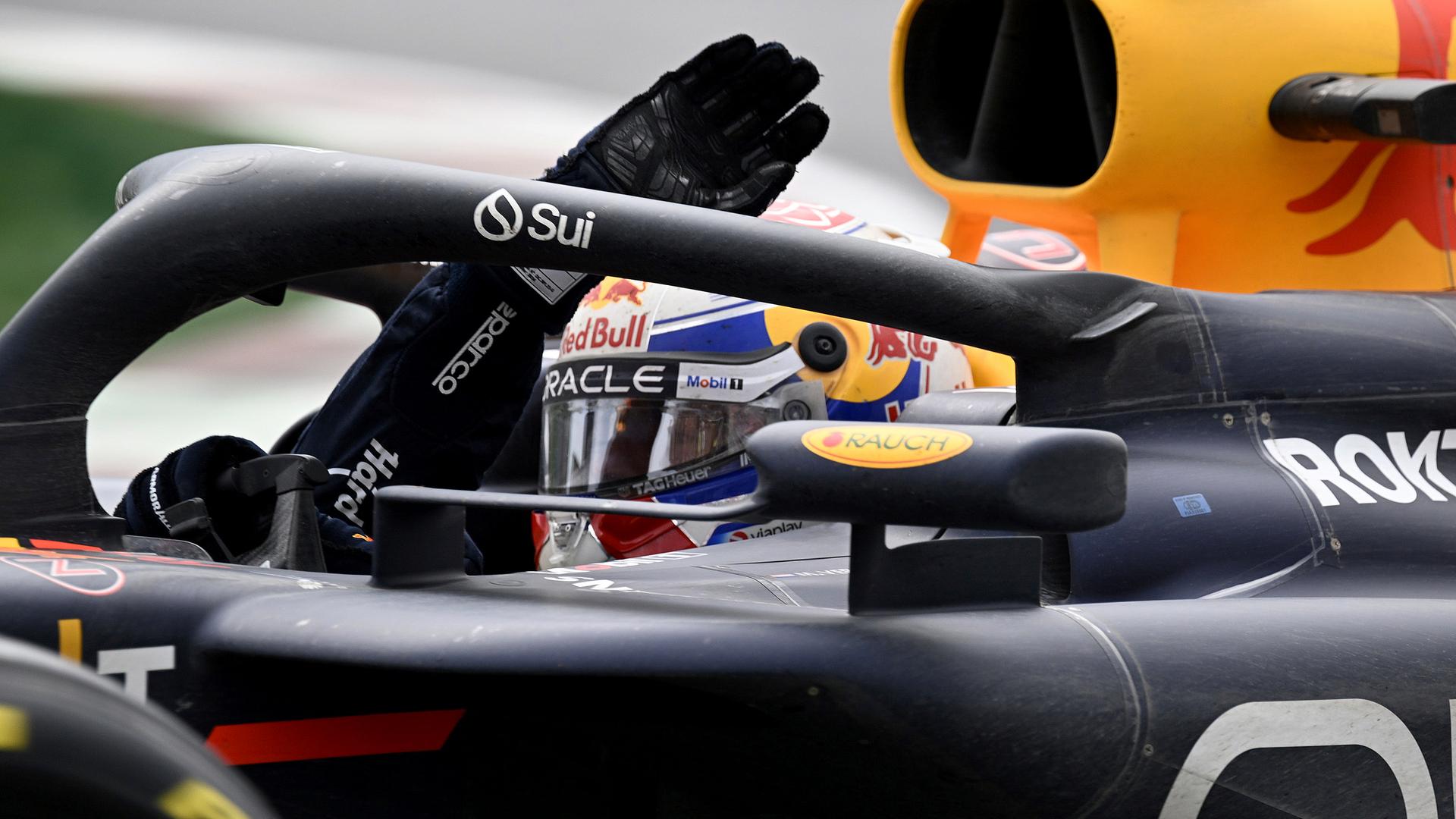 Max Verstappen sitzt in seinem Red-Bull-Fahrzeug und winkt. Max Verstappen sitzt in seinem Red-Bull-Fahrzeug und winkt.