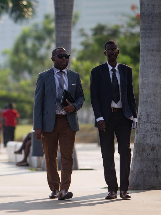 Zwei Geschäftsleute spazieren entlang der Bucht von Luanda in der Nähe der Avenida 4 de Fevereiro. 