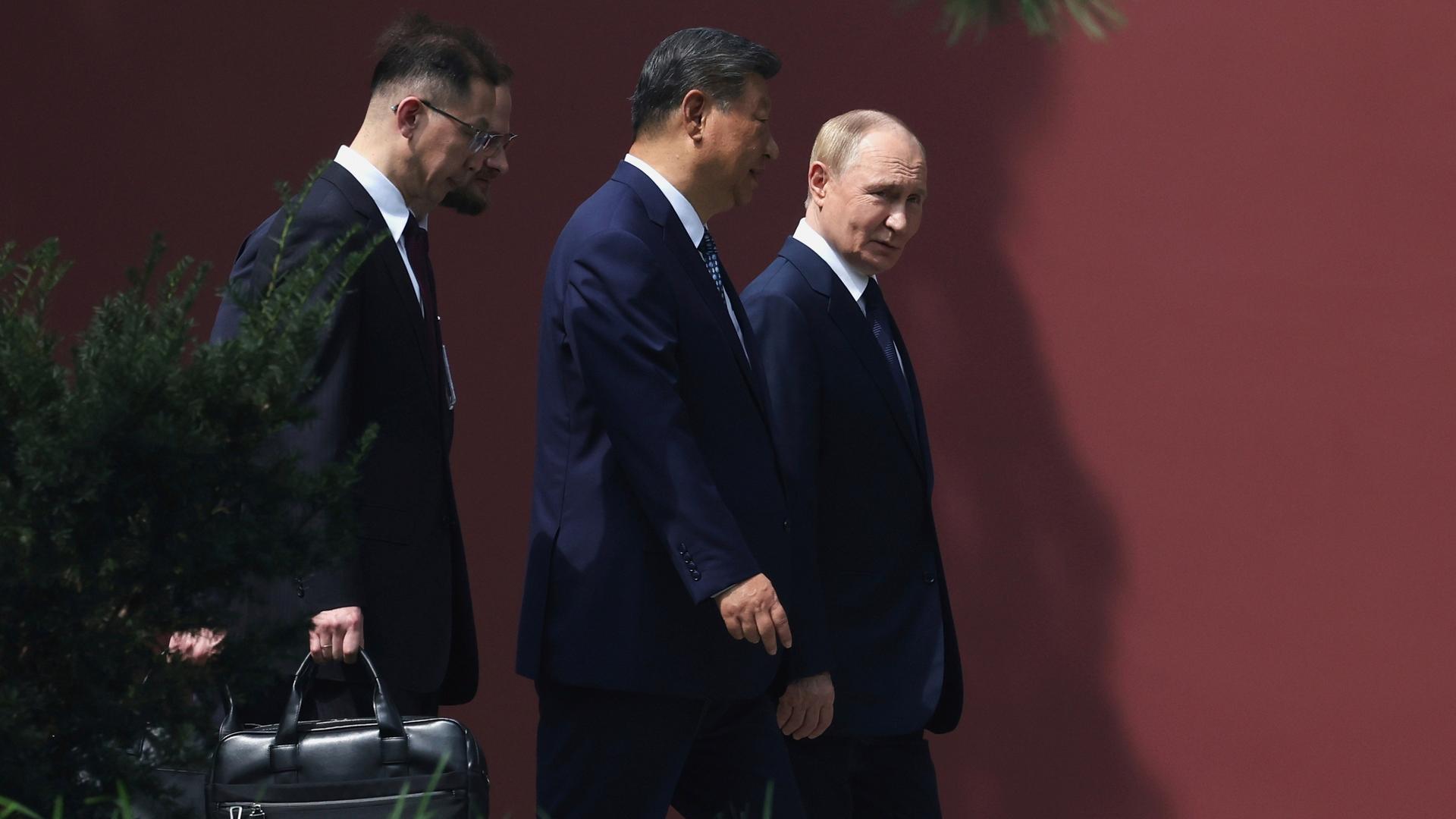 Der russische und der chinesische Präsident Putin und Xi Jinping gehen nebeneinander, hinter ihnen ein Mann, der eine Tasche trägt.