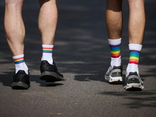 Das Foto zeigt zwei Beinpaare von hinten, die in weißen Socken mit Regenbogen-Bündchen stecken.