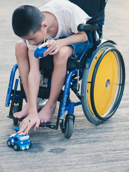 Ein Junge im Rollstuhl setzt ein ferngesteuertes Auto auf den Boden.