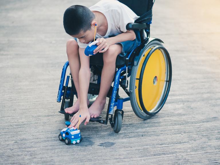 Ein Junge im Rollstuhl setzt ein ferngesteuertes Auto auf den Boden.