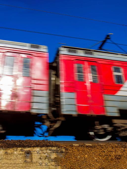 Zwei fahrende rote Waggons der Transsibirischen Eisenbahn auf einem Gleis. Sie fahren, dadurch hat das Bild eine Bewegungsunschärfe.