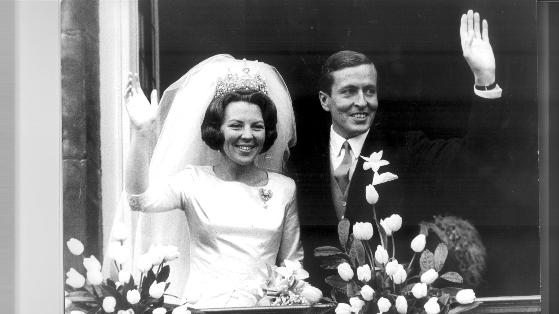 Prinzessin Beatrix von den Niederlanden heiratet den Baron Claus von Amsberg, dann Prinz Claus. Die Braut, links im Foto, träge ein weißes Kleid, der Bräutigam ein dunkles Sakko und Krawatte. Beide winken mit einer Hand.