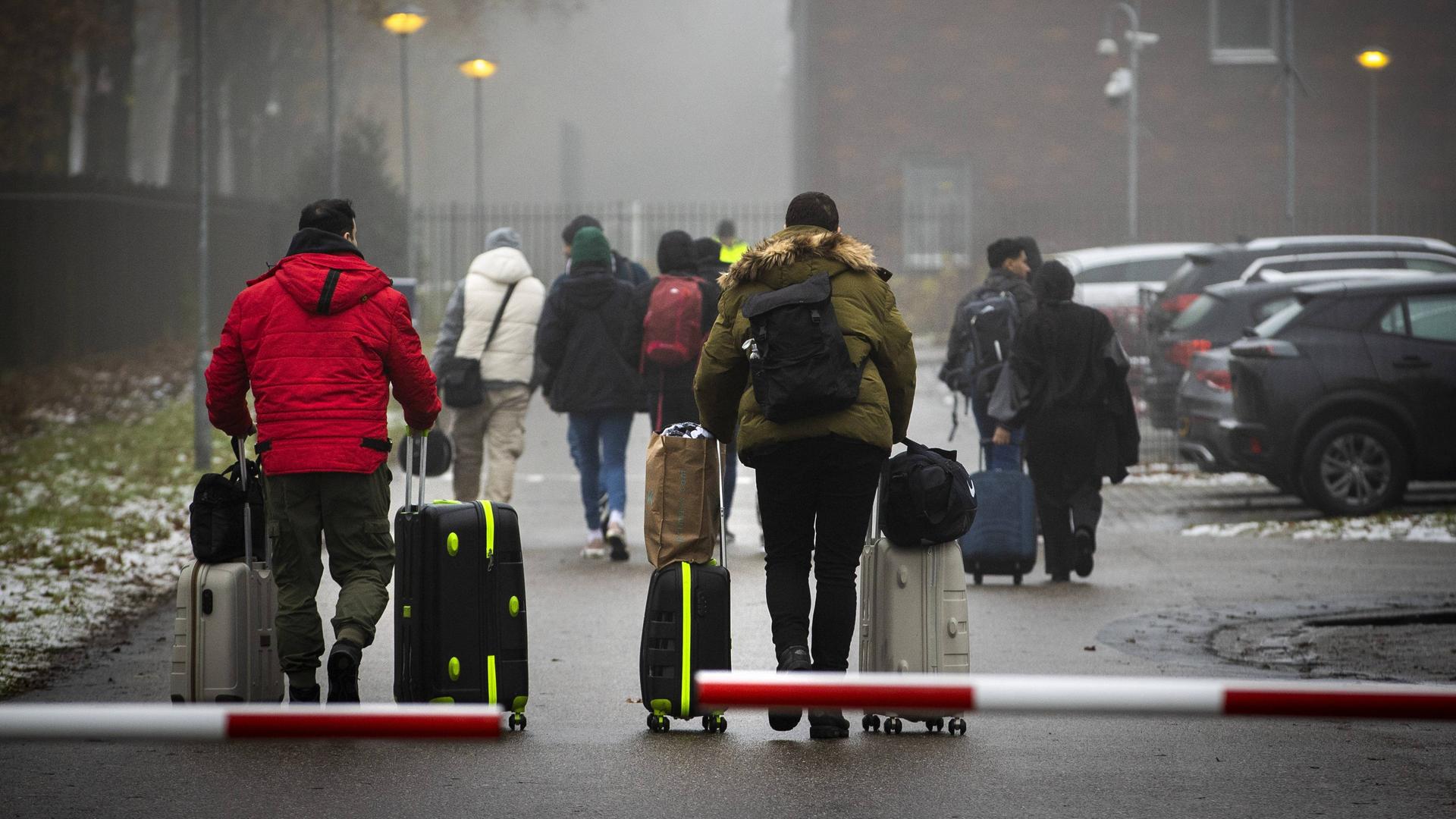 Menschen mit Koffern kommen im niederländischen Asylzentrum Ter Apel an. Sie gehen durch eine Schranke. Menschen mit Koffern kommen im niederländischen Asylzentrum Ter Apel an. Sie gehen durch eine Schranke.